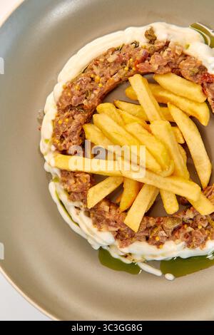 Ein Gourmet-Gericht mit Lagen von herzhaftem Fleisch, umgeben von cremiger Sauce, begleitet von goldenen Pommes Frites, die kunstvoll auf einem Teller angeordnet sind Stockfoto