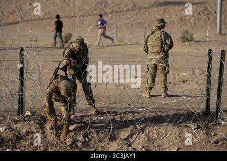 Soldaten patrouillieren einen Stacheldrahtzaun in der Nähe von Ciudad Juarez und überwachen die Grenzsicherheit inmitten von Zivilbewegungen. Stockfoto