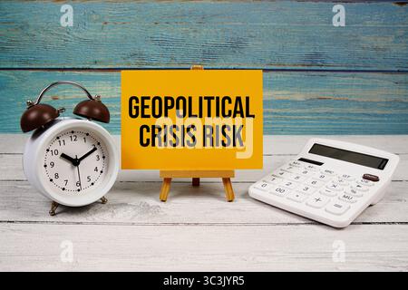 Geopolitischer Krisenrisikotext auf Papierkarte mit Taschenrechner und Wecker auf hölzernem Hintergrund geschrieben Stockfoto