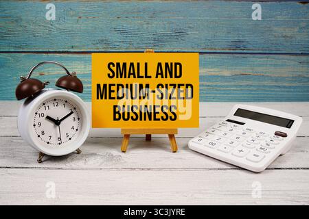 SMB Small and Medium-Sized Business text written on paper card with calculator and alarm clock on wooden background Stockfoto