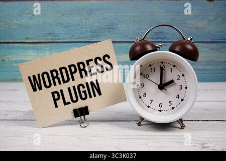 WordPress Plugin Text geschrieben auf Papierkarte mit Wecker auf hölzernem Hintergrund Stockfoto