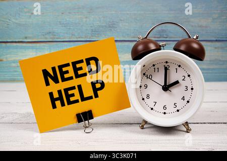 Hilfetext auf Papierkarte mit Wecker auf hölzernem Hintergrund Stockfoto