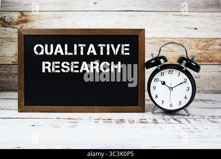 Qualitative Forschung Textnachricht und Wecker auf hölzernem Hintergrund Stockfoto