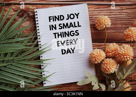 Finde Freude in kleinen Dingen jeden Tag Textnachricht mit Blumendekoration auf hölzernem Hintergrund Stockfoto