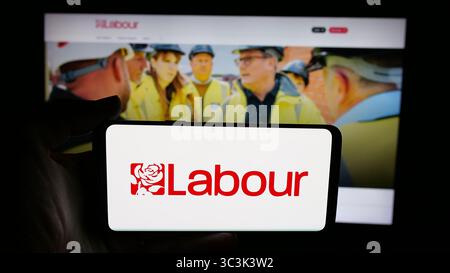 In dieser Fotoabbildung hält eine Person ein Handy mit dem Logo der britischen Partei Labour Party auf dem Bildschirm vor der Webseite. Stockfoto