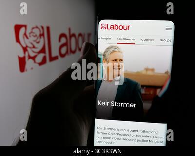 In dieser Fotoabbildung hält eine Person ein Handy mit der Webseite der britischen Partei Labour Party vor dem Logo. Stockfoto