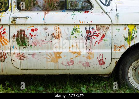 Weiße Autotür mit bunten Handabdrücken und Farbspritzern. Kreatives Kunstprojekt an einer alten Fahrzeugaußenseite. Stockfoto