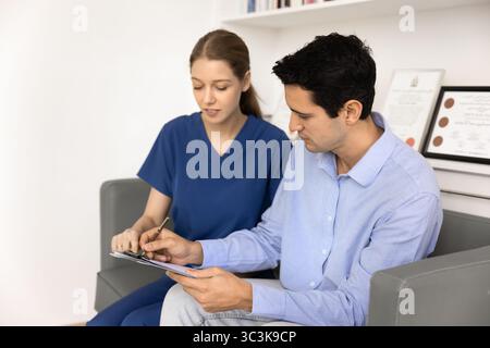 Junge Ärztin in blauen Peelings hilft dem Patienten, die Anwendung zu füllen Stockfoto