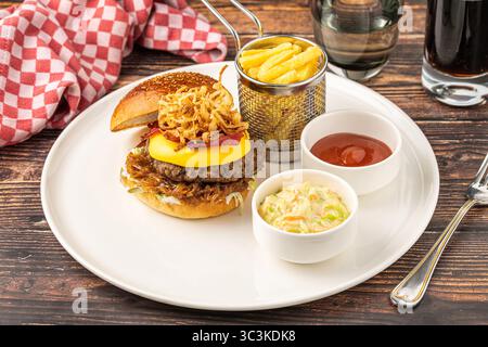 Köstlicher Gourmet-Burger mit Cheddar-Käse, gebratenen Zwiebeln, Krautsalat und Pommes frites Stockfoto