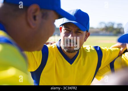 Männliche Baseball-Teamkollegen drängen sich an Baseball-Diamanten in gelben Trikots und blauen Kappen Stockfoto