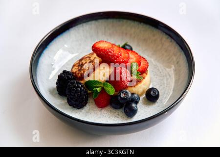 Ein köstlicher Teller flauschiger Pfannkuchen, garniert mit frischen Erdbeeren, Himbeeren, Brombeeren, Heidelbeeren und mit lebendigen Minzblättern Stockfoto