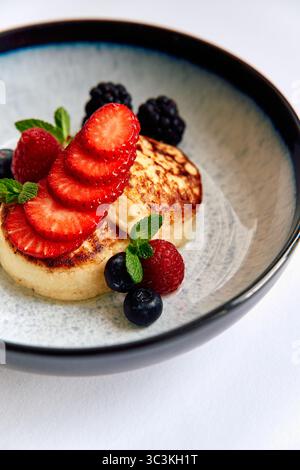 Köstliche Pfannkuchen serviert mit frischen Beeren und Minzblättern in einer stilvollen Schüssel für ein perfektes Frühstückserlebnis Stockfoto