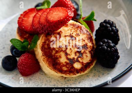 Ein herrlicher Teller flauschiger Pfannkuchen mit frischen Beeren, einschließlich Erdbeeren, Himbeeren und Heidelbeeren, garniert mit Minzblättern für A Stockfoto