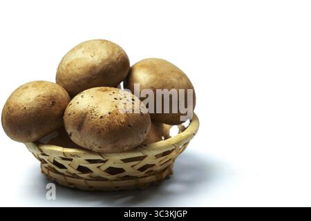 Nahaufnahme von royalbraunen Pilzen, die über einen kleinen gewebten Korb fließen, betonen Frische und Erdtöne vor einem sauberen weißen Hintergrund Stockfoto