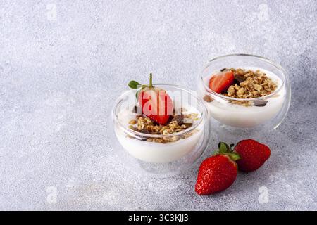 Zwei Glasbecher mit Müsli, Joghurt, Schokolade, frischen Erdbeeren und Kopierraum Stockfoto