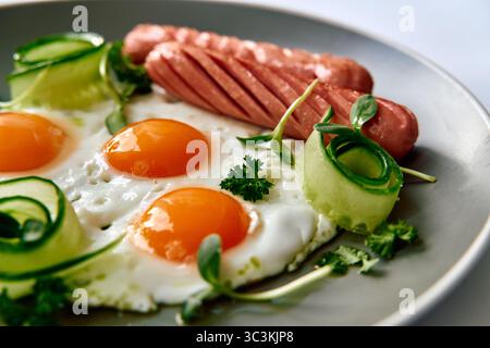 Köstlicher Frühstücksteller mit sonnigen Eiern und Würstchen, begleitet von frischem Gemüse für einen nahrhaften Start in den Tag Stockfoto