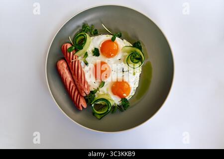 Ein schmackhafter Frühstücksteller mit sonnigen Eiern, Wurst und frischem Gemüse auf einem stilvollen grauen Teller Stockfoto