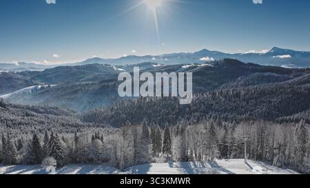 Helle Sonne, die über wunderschönen schneebedeckten Hügeln und Tälern der Karpaten strahlt, mit einem klaren blauen, sonnigen Himmel. Skigebiet Bukovel. Winter wilde Natur Reise Hintergrund Stockfoto