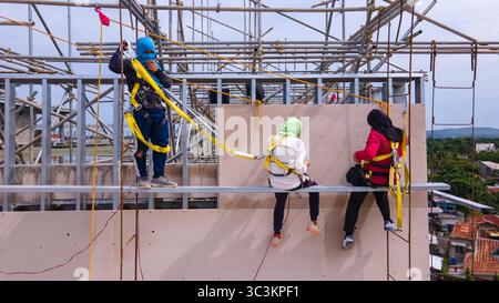 Bauarbeiter installieren Fassadenpaneele in den oberen Ebenen eines Stahlrahmengebäudes, die in der Höhe mit Sicherheitsgurten arbeiten Stockfoto