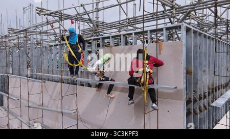 Bauarbeiter installieren Fassadenpaneele in den oberen Ebenen eines Stahlrahmengebäudes, die in der Höhe mit Sicherheitsgurten arbeiten Stockfoto