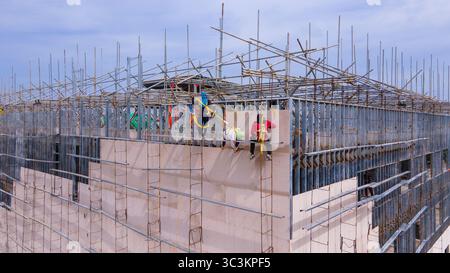 Bauarbeiter installieren Fassadenpaneele in den oberen Ebenen eines Stahlrahmengebäudes, die in der Höhe mit Sicherheitsgurten arbeiten Stockfoto