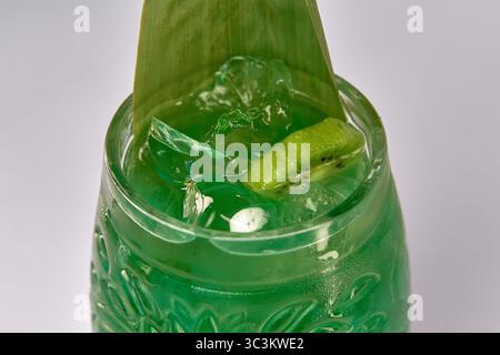 Vibrierender grüner Cocktail in einem dekorativen Glas mit Eis, einer Scheibe Kiwi und einer faszinierenden Garnitur, perfekt für erfrischende Sommermomente. Stockfoto