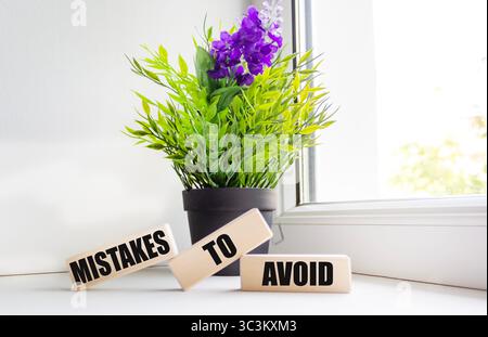 Eine Botschaft, die man vermeiden sollte, ist auf Holzblöcken in einer Komposition mit einer Pflanze auf der Fensterbank geschrieben. Stockfoto