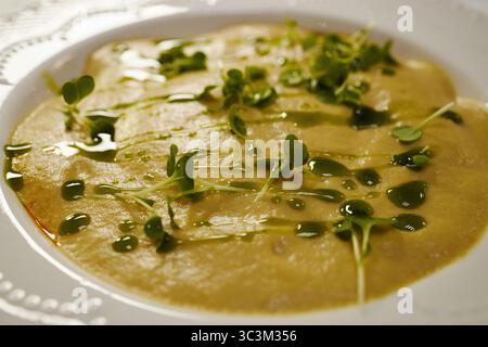 Die Nahaufnahme zeigt cremige Suppe garniert mit frischem Mikrogrün und mit grünem Öl auf dem Teller, wobei der Schwerpunkt auf glatter Textur und lebendiger Präsentation für kulinarische Themen liegt Stockfoto