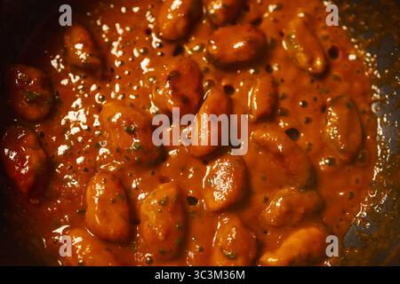 Nahaufnahme mit gekochten Kidneybohnen, die in dicker Tomatensoße mit sichtbaren Kräutern kochen, wodurch die Textur und das glänzende Aussehen von Bohnen in reichhaltiger Soße hervorgehoben werden Stockfoto