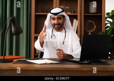 Arzt aus dem Nahen Osten mit emirat Kandura im Büro - zuversichtlicher Kardiologe in traditioneller emiratischer Kleidung in einem modernen dubai o Stockfoto