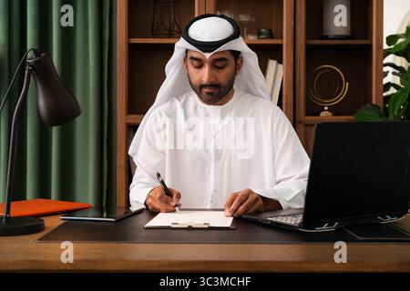 Geschäftsmann aus dem Mittleren Osten trägt emirat Kandura, der im Büro arbeitet - Geschäftsmann aus dem Mittleren Osten in traditionellem emirat Kandura, der mich unterzeichnet Stockfoto