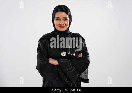 Selbstbewusst lächelnde muslimische Ärztin, die eine traditionelle schwarze Abaya und Hijab trägt, zeigt die Professionalität der Gesundheitsfürsorge im Nahen Osten Stockfoto