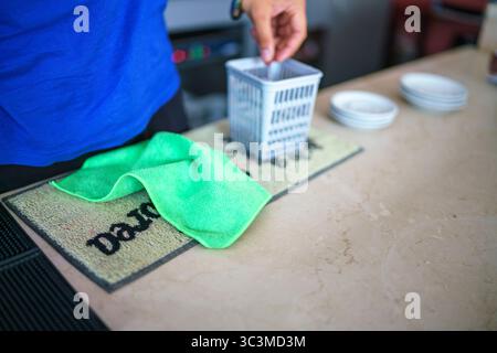 Cremona, Italien - 25. Juli 2025 Nahaufnahme einer Person, die eine Arbeitsplatte mit einem Mikrofasertuch und einem kleinen Korb für die Reinigung von Zubehör reinigt Stockfoto
