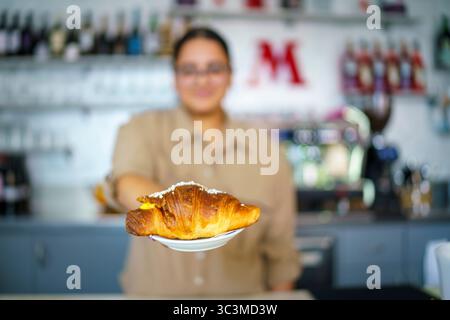 Cremona, Italien - 25. Juli 2025 Friendly Barista bietet köstliche goldene Croissants auf einem Teller in gemütlicher Café-Atmosphäre Stockfoto