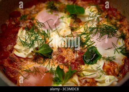 Ein köstliches Shakshuka-Gericht mit pochierten Eiern in einer scharfen Tomatensauce, garniert mit frischen Kräutern und Gemüse für eine geschmackvolle Mahlzeit Stockfoto
