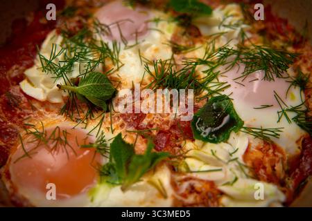 Ein köstlich garniertes Shakshuka-Gericht mit hellem Eigelb, frischen Kräutern und einer aromatischen Tomatenbasis, die das kulinarische Erlebnis bereichert Stockfoto