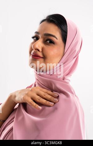 Studio-Porträt einer wunderschönen arabischen Frau in einem rosa Hijab, das eine Mischung aus Tradition, Anmut und moderner Mode in einem minimalistischen Ambiente zeigt Stockfoto