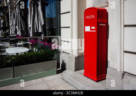 Warschau, Polen - 2. Juli 2025: Traditioneller roter Briefkasten in der Nähe eines Cafés in Warschau, Polen mit Blumendekor Stockfoto