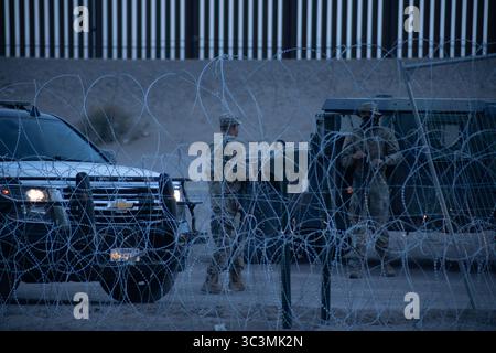 Soldaten patrouillieren in der Abenddämmerung in der Nähe von Stacheldrahtzäunen entlang der befestigten Grenze von Ciudad Juarez, was die Migrationsspannungen hervorhebt. Stockfoto