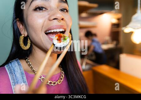 Eine Frau genießt ein Stück Sushi und benutzt gekonnt Essstäbchen, um ihr Essen in einem Restaurant zu genießen. Das Ambiente strahlt Wärme aus und verleiht dem Essen eine besondere Note Stockfoto