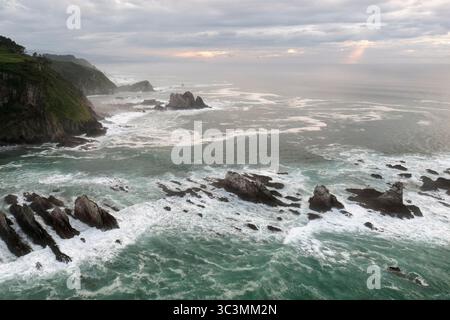 Ein ruhiger Blick auf den ruhigen Strand in Asturien, Spanien, mit zerklüfteten Klippen und turbulenten Wellen, die eine malerische und ruhige Küstenlandschaft schaffen Stockfoto