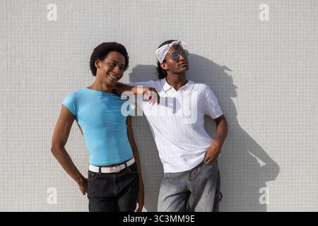 Ein fröhliches, queeres Paar sorglos und entspannt, lehnt sich an einem hellen Sommertag an eine gekachelte Wand und genießt die Wärme und die Gesellschaft. Stockfoto