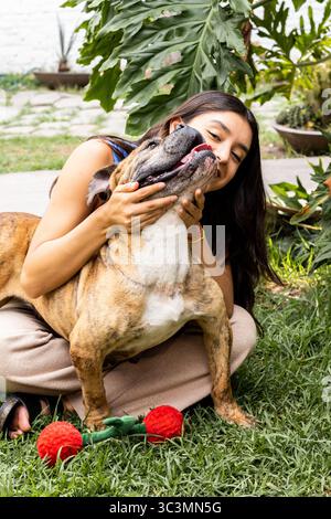 Eine Frau umarmt ihren adoptierten Hund in einem üppigen Garten. Die Verbindung zwischen ihnen ist offensichtlich, da sie einen glücklichen Moment teilen, umgeben von greene Stockfoto