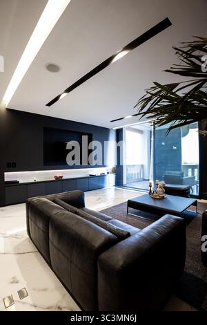 Geräumiges Wohnzimmer mit moderner Eleganz, elegantem Schwarz-weiß-Dekor, komfortablem Ledersofa, stilvollem Couchtisch und großem Fenster für Stockfoto