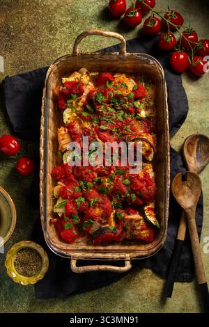 Ein Gourmet-Gericht mit gebackenem Lachs, perfekt kombiniert mit einer bunten Mischung aus Gemüse in einer reichhaltigen und aromatischen Tomatensauce, garniert mit frischem HE Stockfoto