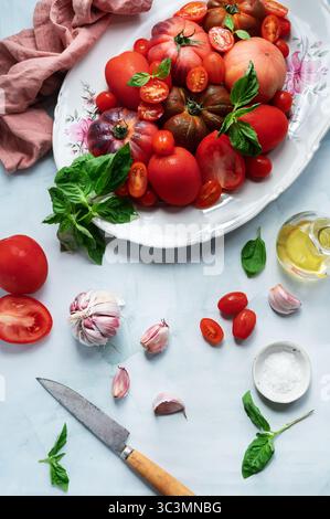 Eine lebhafte Auswahl an frischen Tomaten, Knoblauch, Basilikumblättern, Olivenöl und Meersalz, die wunderbar für die Zubereitung einer köstlichen kalten Tomatensuppe auf Hom zubereitet werden Stockfoto