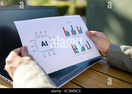 Eine Transfrau, die draußen arbeitet und Datendiagramme auf Papier untersucht. Die Einrichtung ist professionell, mit einem Laptop auf einem Holztisch, hervorgehoben Arbeiten und einem Stockfoto