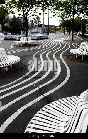 Künstlerischer Blick auf den Superkilen Park in Kopenhagen mit fließenden weißen Linien auf schwarzem Bürgersteig, modernen weißen Bänken und urbanen Bäumen Stockfoto