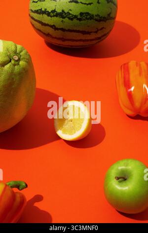Buntes Obst und Gemüse im Pop-Art-Stil auf leuchtend roten Hintergründen. Die verspielte Komposition und die kräftigen Farbtöne sorgen für ein lebendiges, geselliges Ambiente Stockfoto