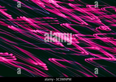 Eine fesselnde Darstellung rosa Lichtspuren bei langer Belichtung, die mystische Muster vor dunklem Nachthintergrund erzeugen. Ideal für die Darstellung von Halloween Stockfoto